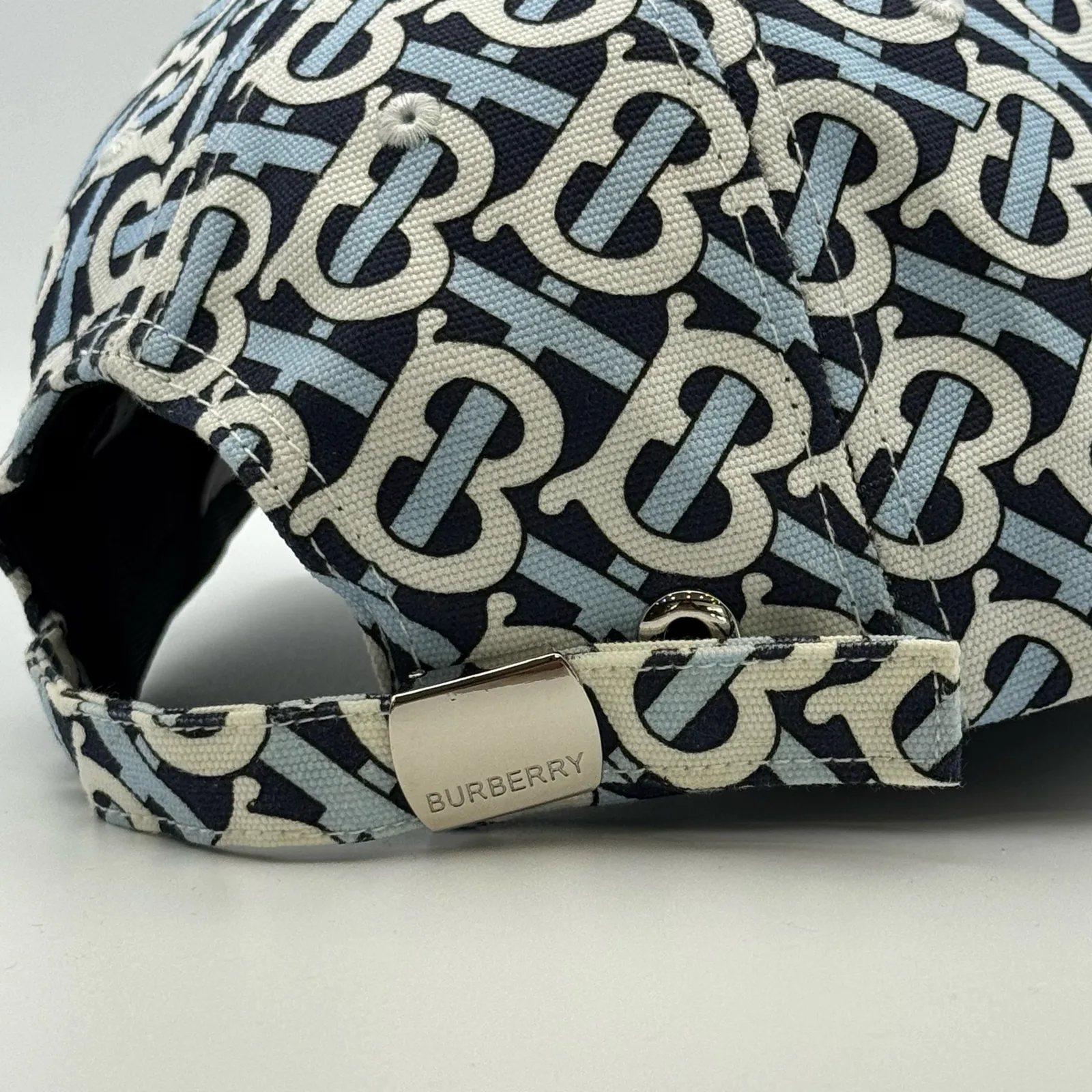 Close-up of the metal Burberry tab on the back strap of the navy monogram cap.