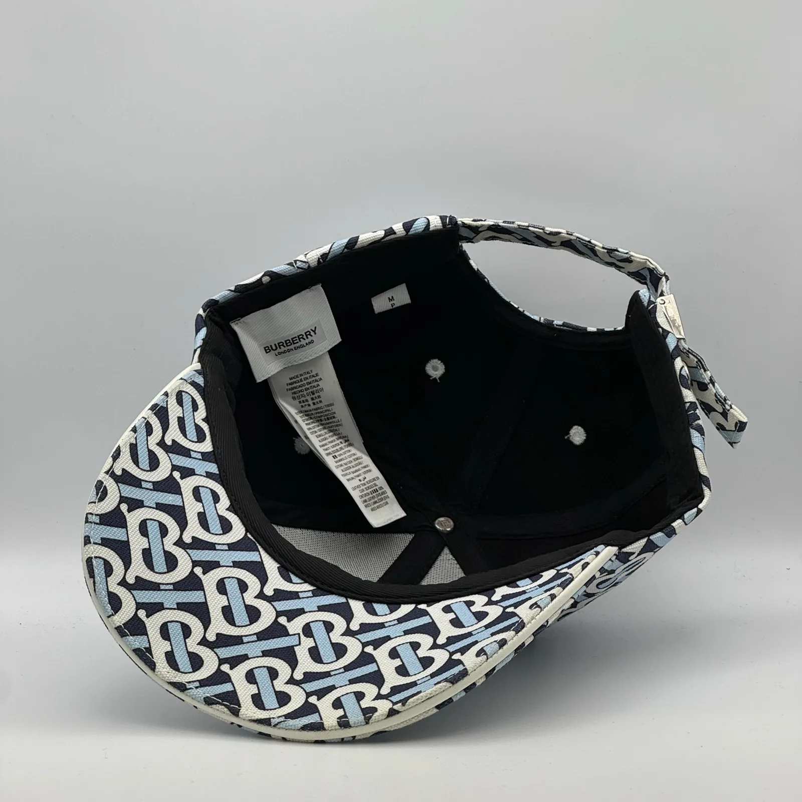 Underside of the navy monogram cap, brim lifted to show the interior and tag.