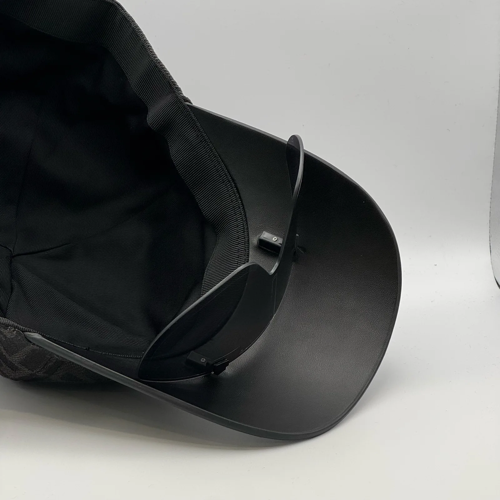 Underside of the black Fendi Visor cap, brim lifted to show the interior strap.