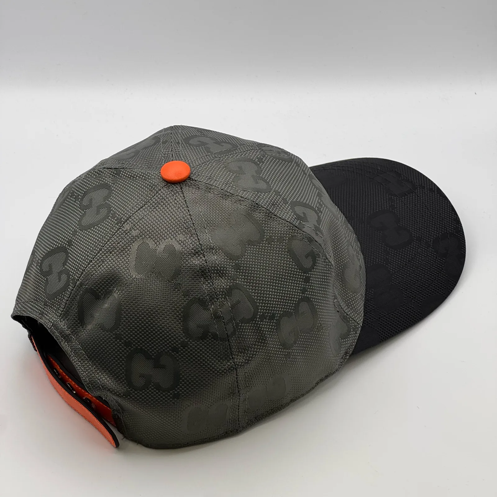 Grey GG cap, three-quarter back view showing orange tab and brim