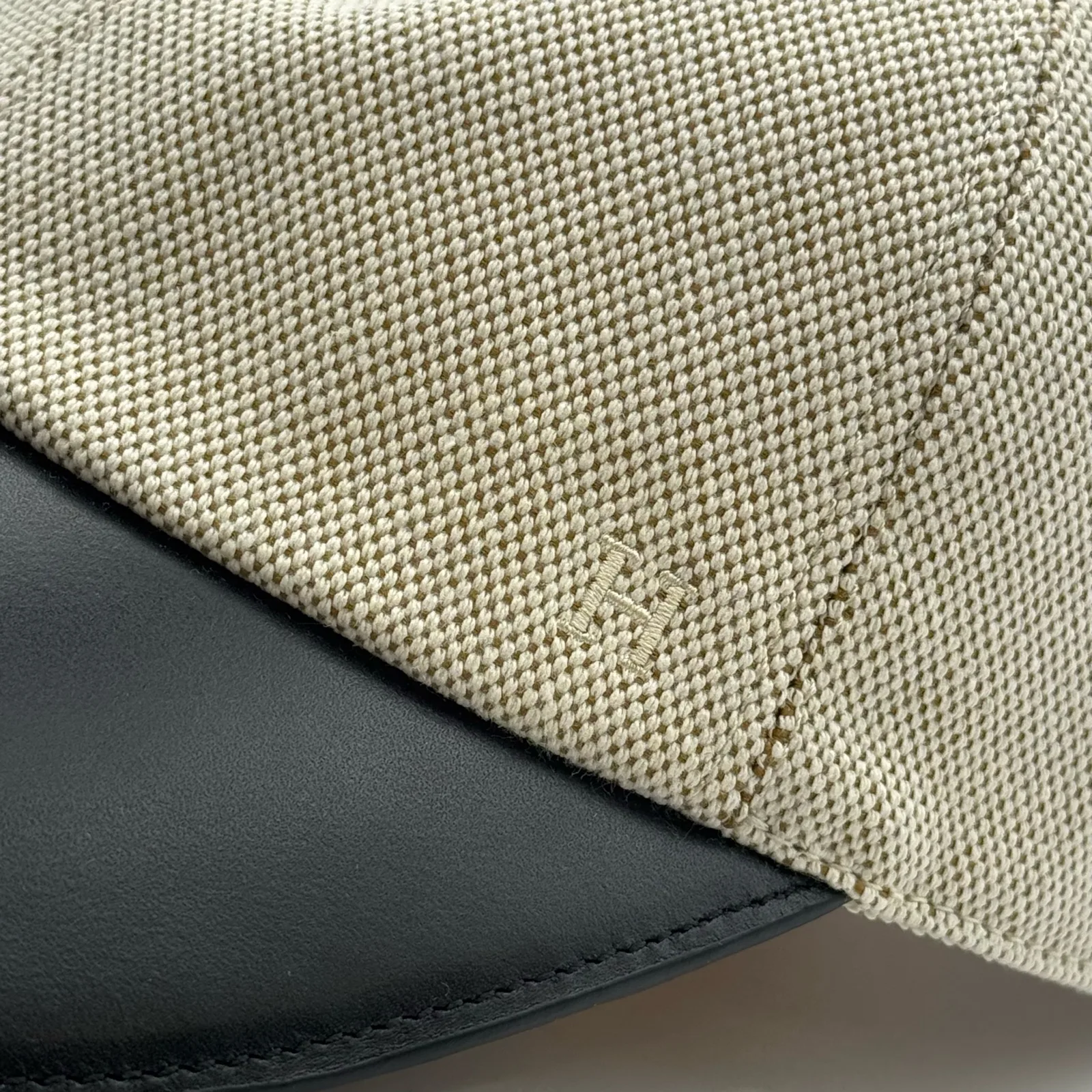 Close-up of the black leather brim meeting the woven canvas crown, with a small tone-on-tone logo.