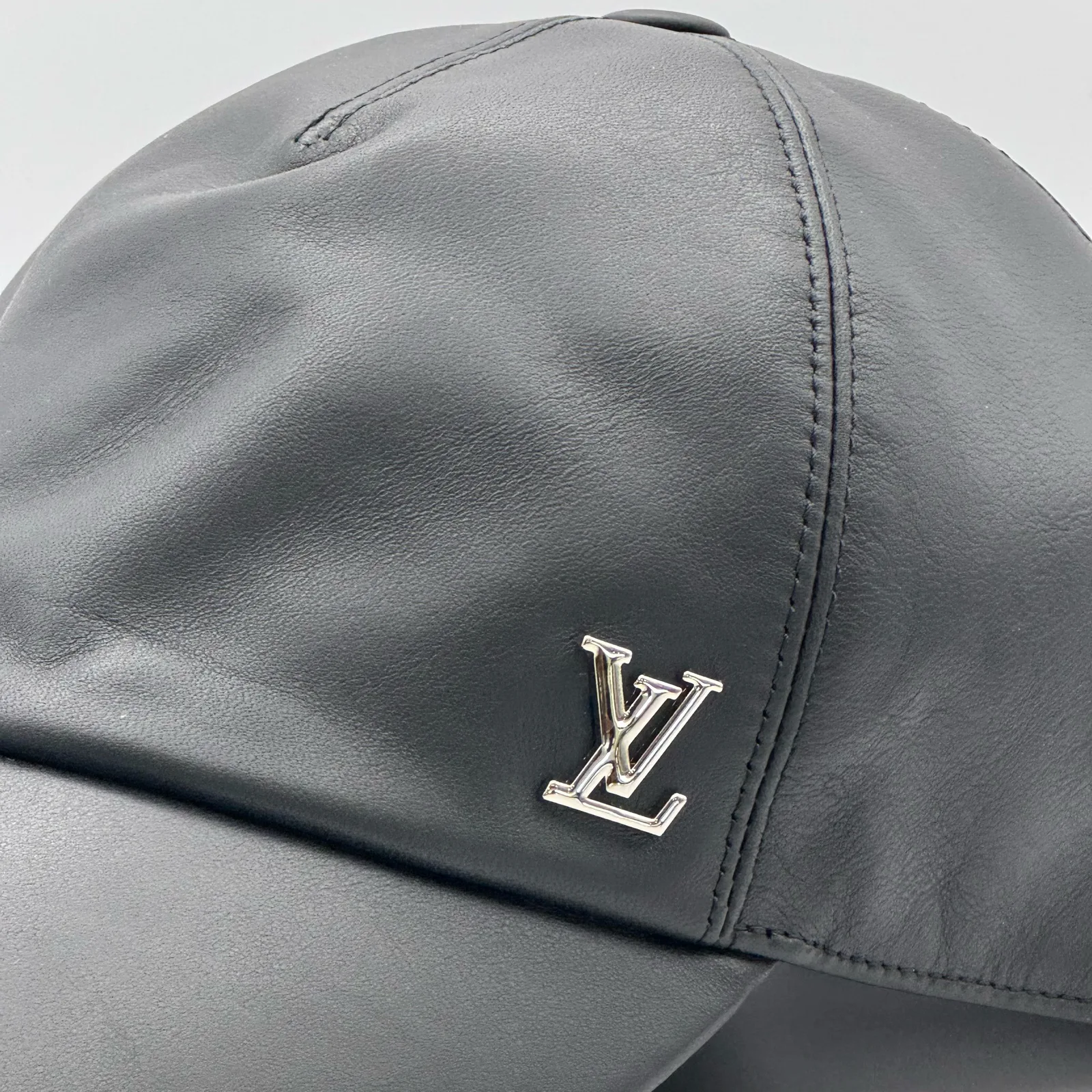 Close-up of the silver-tone LV metal logo on the black leather cap.
