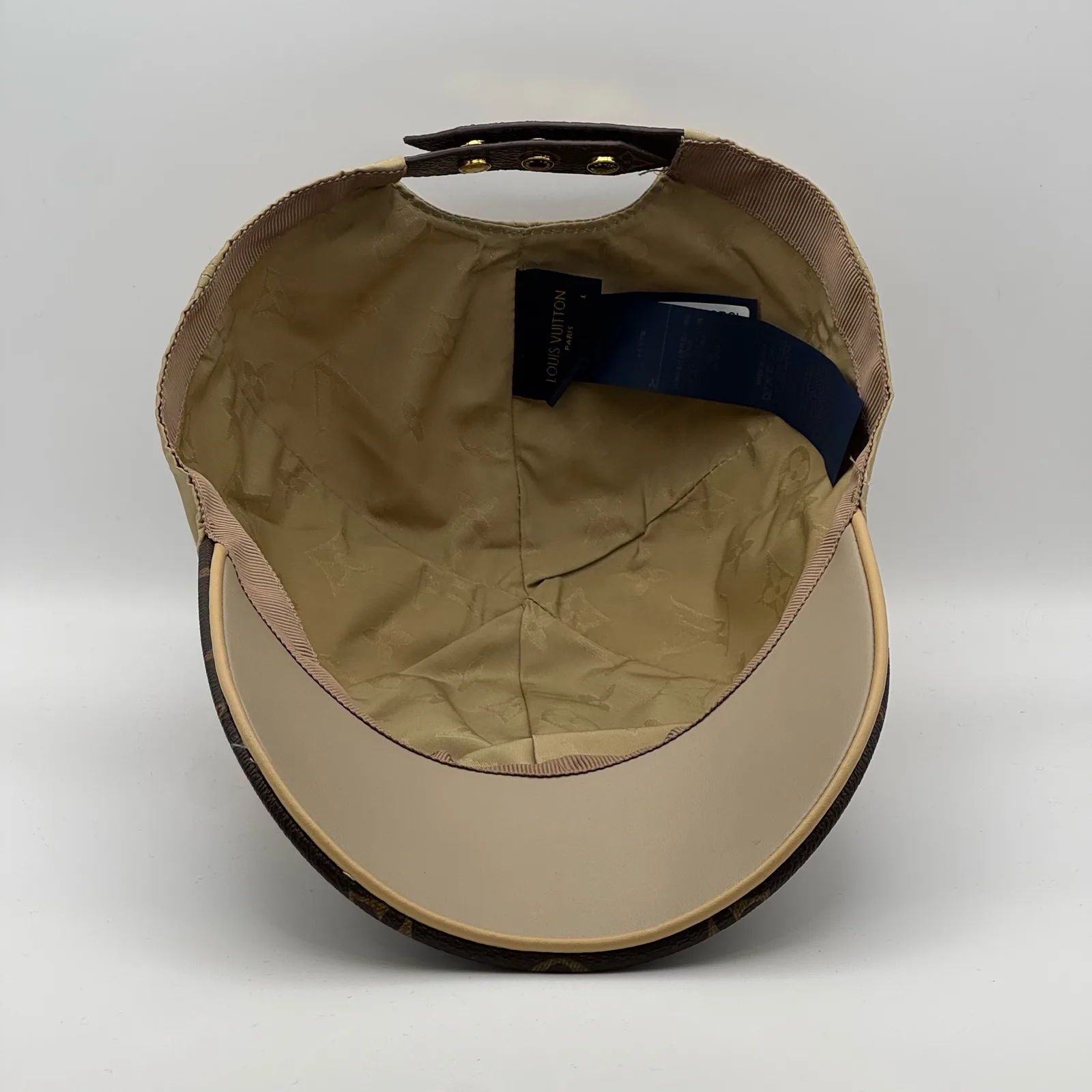Underside view of the beige cap showing the monogram brim lining.