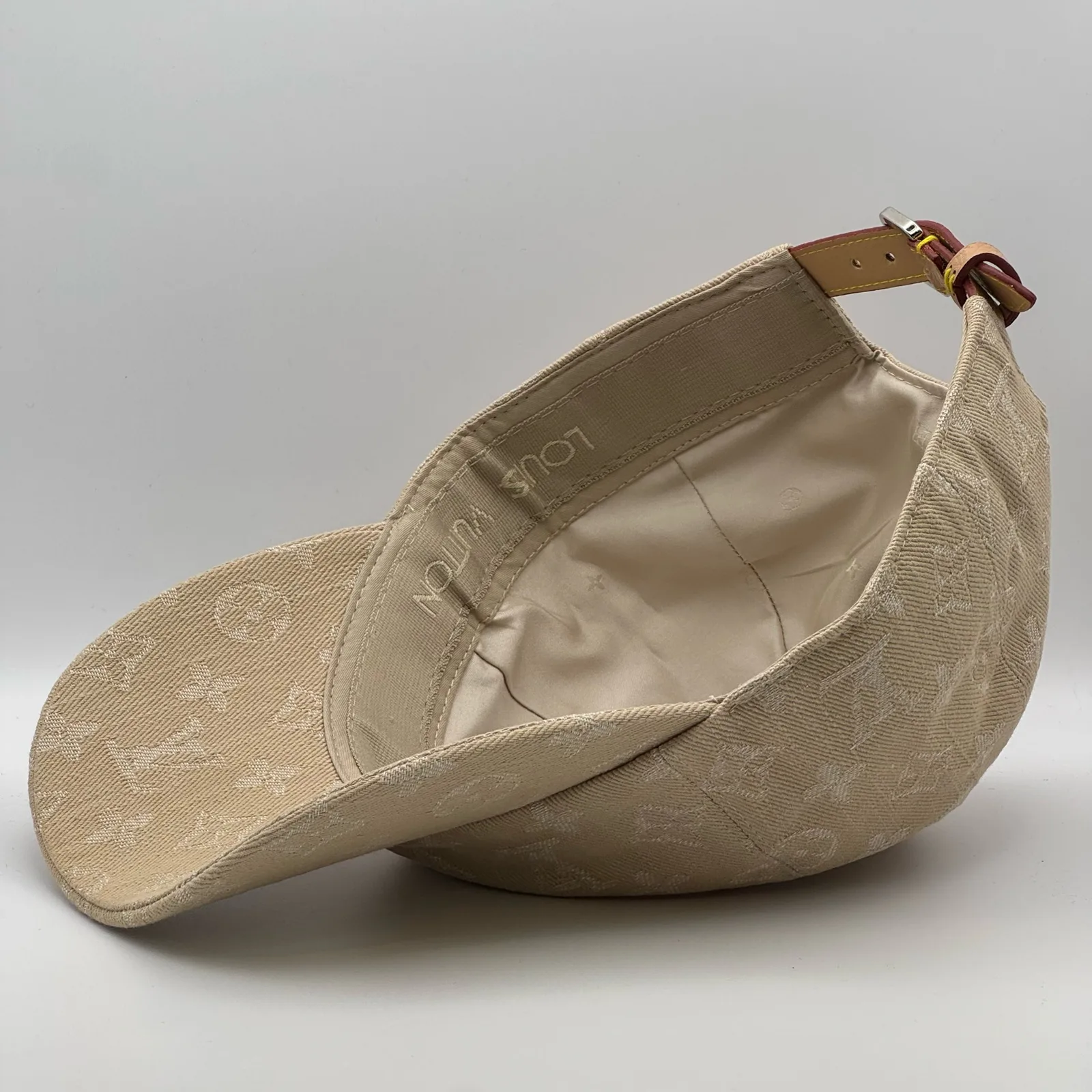 Underside view of the beige cap showing the brim and leather strap.